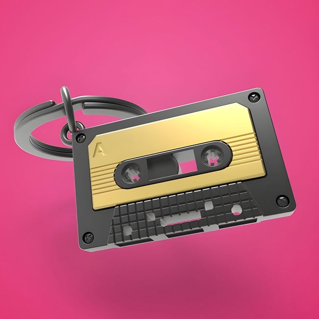 Metalinis raktų pakabukas „Audio Kasetė“ – retro kasetės 3D miniatiūra iš Muzikos Pasaulis kolekcijos. Auksinė ir juoda spalva, mini detalės, plieninis žiedas.