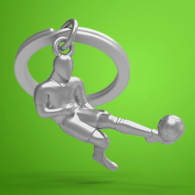 Metalmorphose.lt metalinis raktų pakabukas FUTBOLO ŽAIDĖJAS. 3D futbolininko figūra su kamuoliu, dinamiškas smūgio momentas, premium cinko lydinys, plieno žiedas. Iš SPORTO PASAULIS kolekcijos.