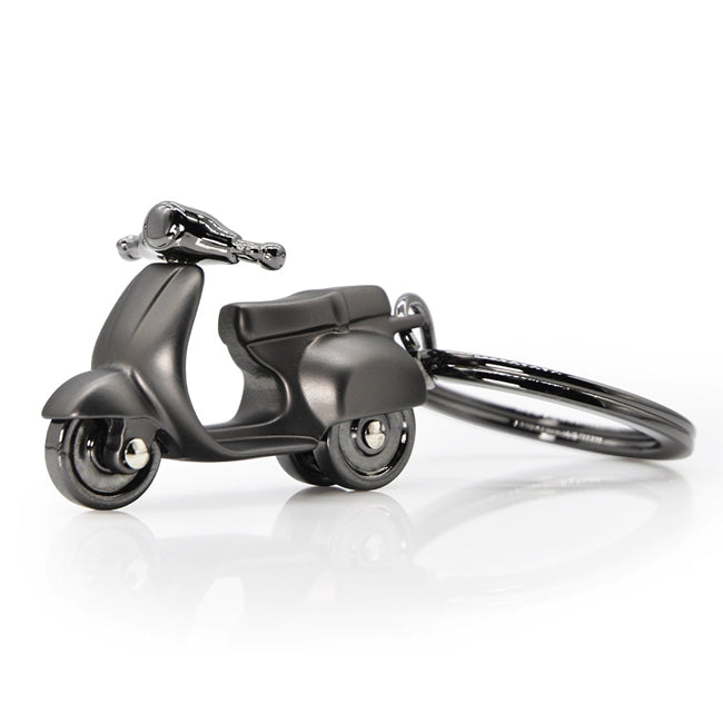 Metalmorphose.lt metalinis raktų pakabukas JUODA PYRDA. Juodas metalinis skuteris su detaliomis rankenėlėmis, kėbulo linijomis ir premium metaliniu žiedu. TRANSPORTO PASAULIS kolekcija.