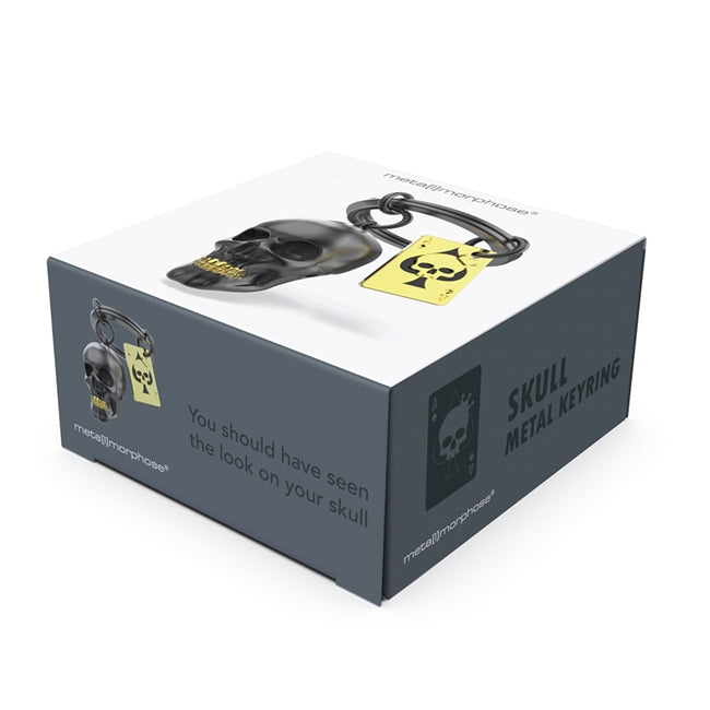 Metalmorphose.lt metalinis raktų pakabukas KAUKOLĖ IR KORTA. Tvirtas metalinis korpusas, juodai nudažyta kaukolė, auksinė korta, detalizuota kaukolės 3D miniatiūra. Nerūdijančio plieno žiedas. Pakabukas iš KASDIENYBĖS PASAULIS kolekcijos.