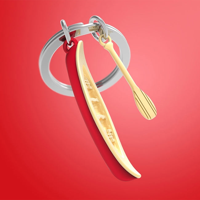 Metalmorphose.lt metalinis raktų pakabukas KANOJOS KELIAS. Raudona kanoja ir auksinis irklas, detalus 3D vandens nuotykių simbolis. Premium cinko lydinys, nerūdijančio plieno žiedas. Pakabukas iš KELIONIŲ PASAULIS kolekcijos.