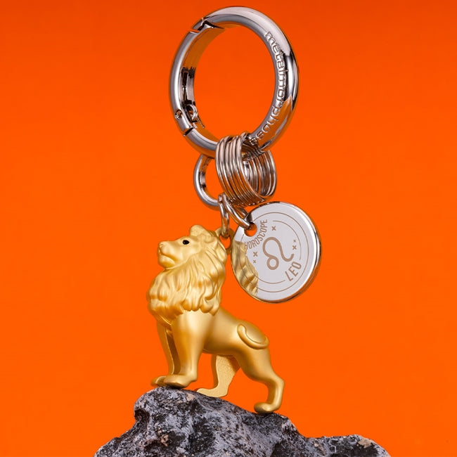 Metalmorphose.lt metalinis raktų pakabukas LIŪTAS. Karališka auksinio liūto galva su detaliais karčiais, saulės ženklo simbolika, premium cinko lydinys ir plieno žiedas. Pakabukas iš ZODIAKŲ PASAULIS kolekcijos.
