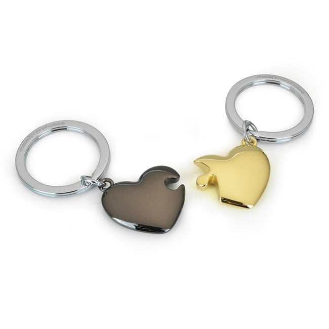 Metalmorphose.lt metalinis raktų pakabukas MEILĖS DĖLIONĖ. Juoda ir auksinė širdys sujungtos kaip dėlionės dalys. Premium metalas. MEILĖS PASAULIS kolekcija.