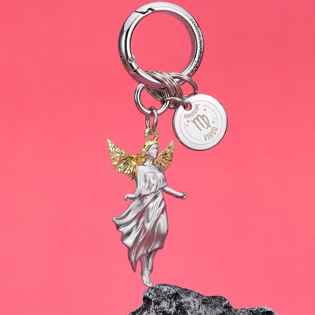 Metalmorphose.lt metalinis raktų pakabukas MERGELĖ. Elegantiška Mergelės figūra, auksiniai sparnai, žemės ženklo simbolika, premium cinko lydinys, plieno žiedas. Pakabukas iš ZODIAKŲ PASAULIS kolekcijos.