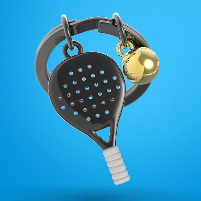 Metalmorphose.lt metalinis raktų pakabukas PADELIO ŠOKIS. Juoda 3D padelio raketė su auksiniu kamuoliuku, detalus cinko lydinio dizainas, plieno žiedas. SPORTO PASAULIS kolekcija.