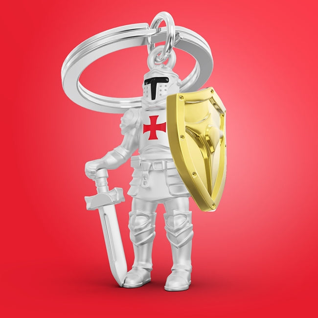 Metalmorphose.lt metalinis raktų pakabukas RITERIS. Tvirtas metalinis korpusas, auksiniai akcentai, nudažytas raudonas kryžius, riterio su kardu ir skydu 3D miniatiūra. Nerūdijančio plieno žiedas. Pakabukas iš KASDIENYBĖS PASAULIS kolekcijos.