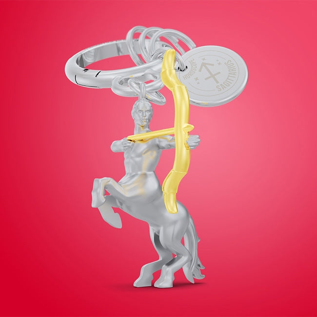 Metalmorphose.lt metalinis raktų pakabukas ŠAULYS. 3D šaulio simbolis, auksinių lanko ir strėlės miniatiūra, ugnies ženklo simbolika, premium cinko lydinys, plieno žiedas. Pakabukas iš ZODIAKŲ PASAULIS kolekcijos.