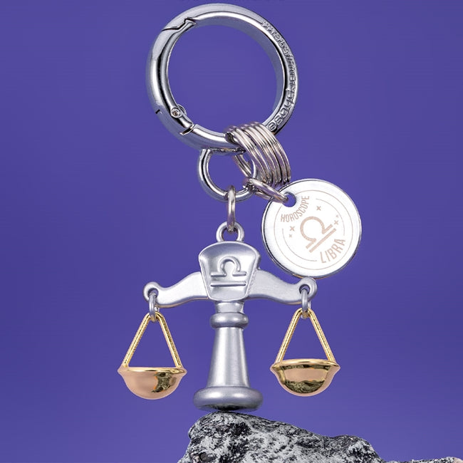 Metalmorphose.lt metalinis raktų pakabukas SVARSTYKLĖS. Delikati svarstyklių miniatiūra, auksinės detalės, oro ženklo simbolika, premium cinko lydinys ir plieno žiedas. Pakabukas iš ZODIAKŲ PASAULIS kolekcijos.