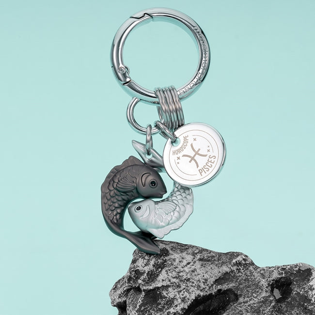 Metalmorphose.lt metalinis raktų pakabukas ŽUVYS. Dvi apsijungusios žuvys, vandens ženklo simbolika, 3D miniatiūra, premium cinko lydinys, plieno žiedas. Pakabukas iš ZODIAKŲ PASAULIS kolekcijos.