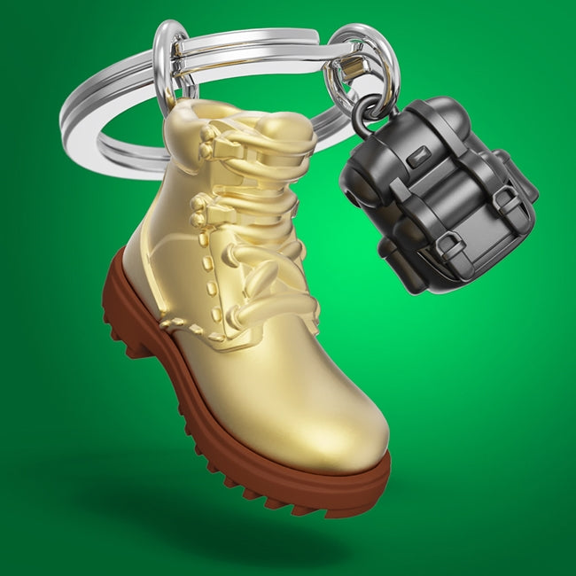 Metalmorphose.lt metalinis raktų pakabukas ŽYGEIVIO ŽINGSNIAI. Auksinis žygio batas ir juoda kuprinė, 3D hiking miniatiūra. Premium cinko lydinys, nerūdijančio plieno žiedas. Pakabukas iš KELIONIŲ PASAULIS kolekcijos.